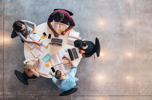 Imagem vista de cima, com uma mesa com cinco estudantes criando uma rotina de estudos
