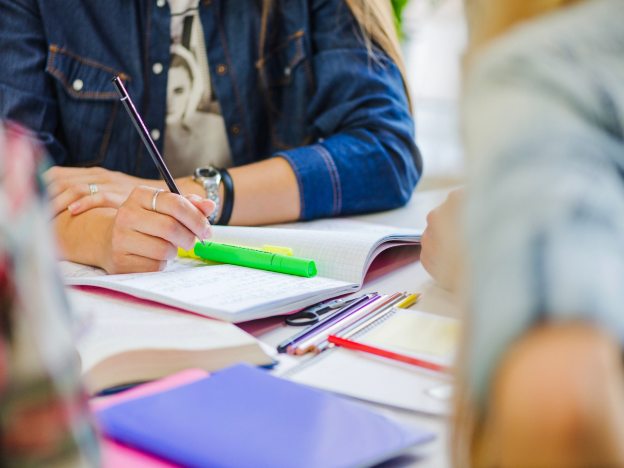 Mulher em uma mesa de estudos com livros, cadernos e canetas ao seu alcance, fazendo anotações e utilizando alguns métodos para estudar para o vestibular.