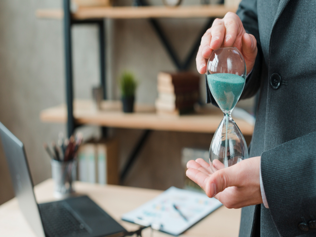 Gestão do tempo: homem de negócios em seu escritório, segurando uma ampulheta.