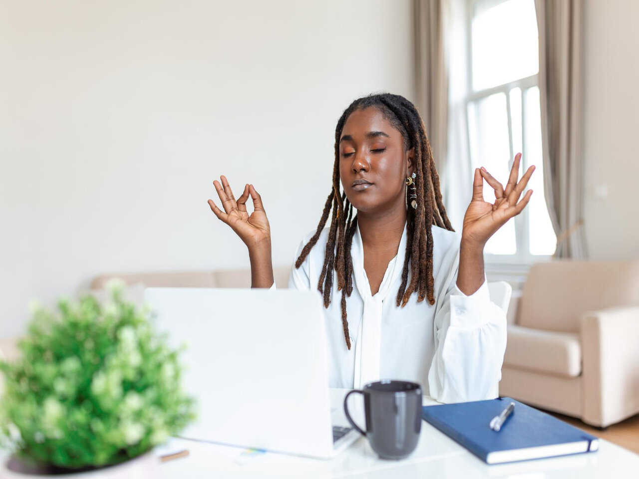 O que é mindfulness: Mulher sentada em frente ao seu computador com materiais de estudos à sua volta. Ela está em posição de meditação, com os cotovelos sobre a mesa e as pontas dos dedos se tocando.
