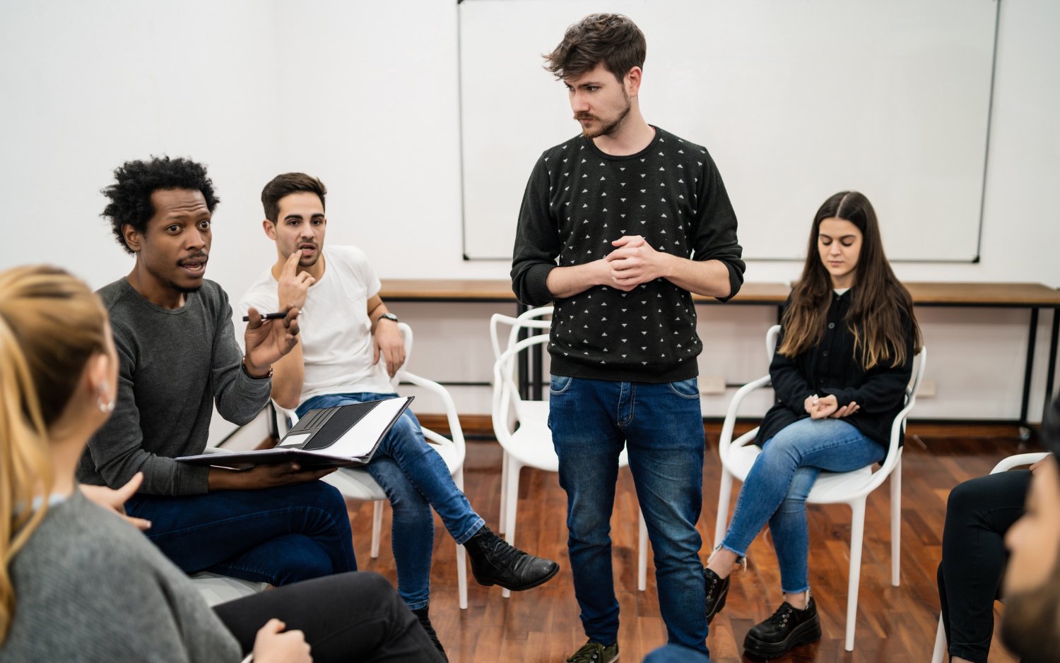 Aluno de pé no centro da sala de aula e rodeado por seus colegas, durante um debate na faculdade