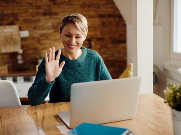 Mulher em um cômodo da casa, utilizando o notebook para participar de uma entrevista online de emprego